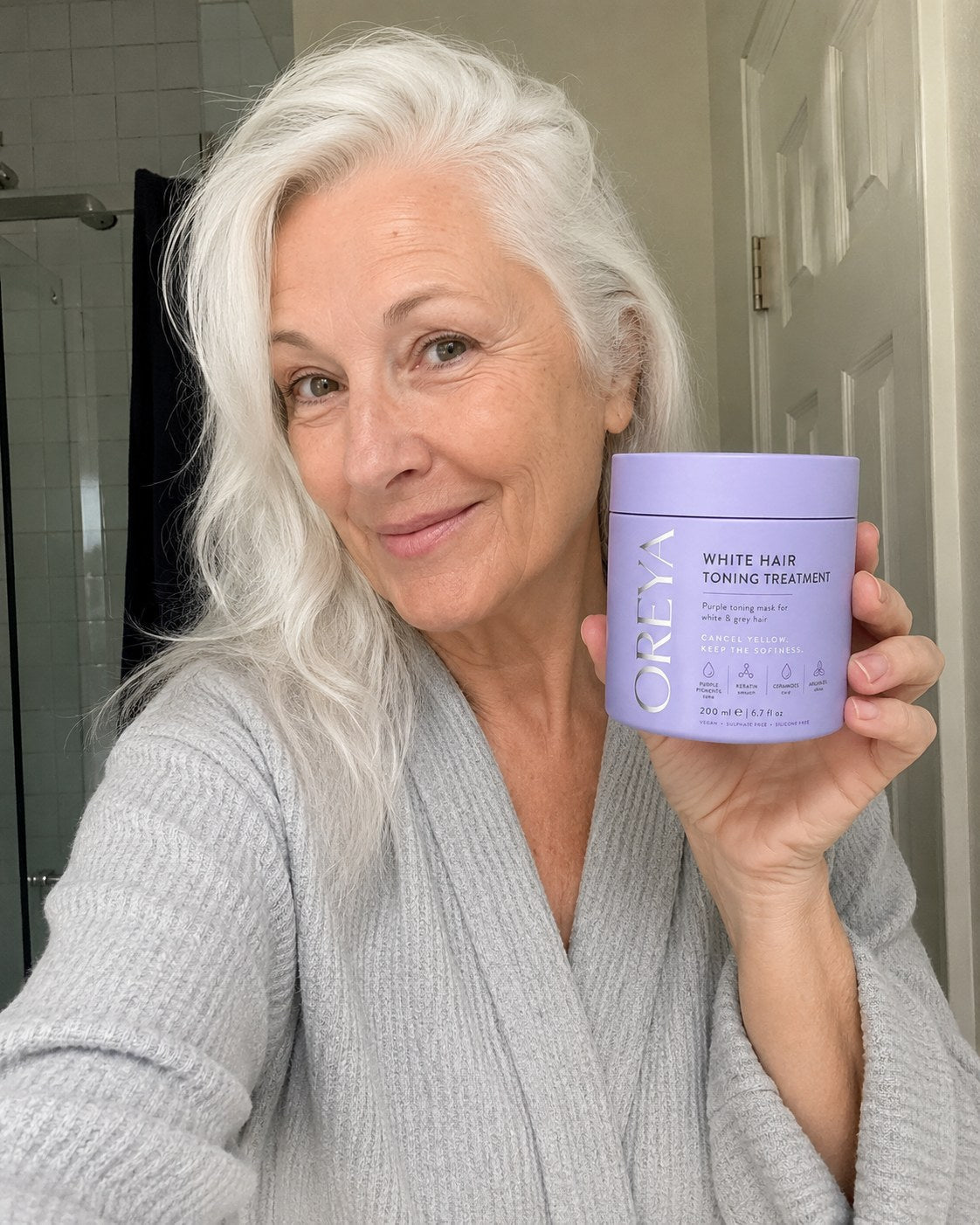 Woman with naturally white hair holding Oreya in a bathroom selfie